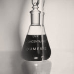 Black and white image of a glass bottle labeled 'OU-MERE' with a dropper on a light background