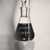 Black and white image of a glass bottle labeled 'OU-MERE' with a dropper on a light background