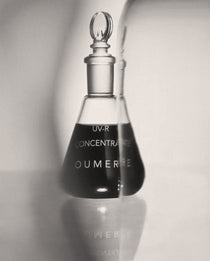 Black and white image of a glass bottle labeled 'OU-MERE' with a dropper on a light background